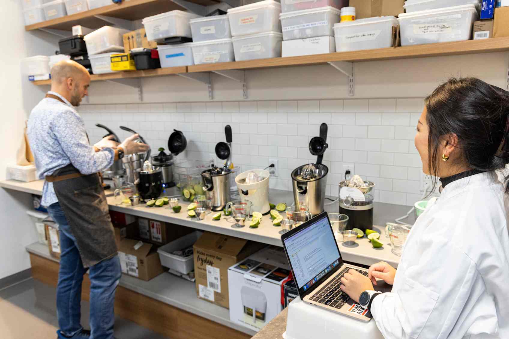 Sam Treadway uses an electric citrus juicer to extract lime juice while Valerie Sizhe Li takes notes on her laptop. 